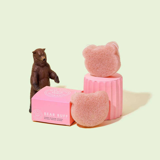 A pink Konjac sponge shaped like a bear, displayed next to its packaging box with a bear figurine.